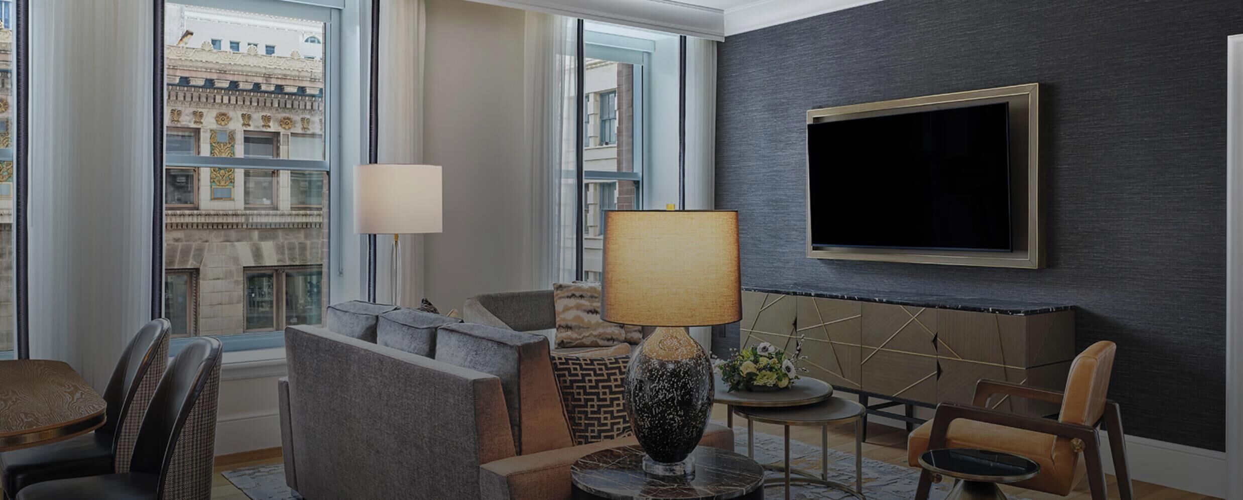 Een moderne woonkamer met een bank, fauteuils, een salontafel, een lamp en een televisie aan de muur.