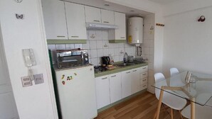 Eine kompakte Küche mit weißen Schränken, einem eingebauten Backofen, einem Spülbecken und einem Glastisch mit Stühlen.