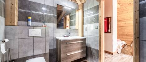Et moderne badeværelse med træloft, grå fliser, et hvidt toilet, et spejl med vaskebord og et bruseområde.