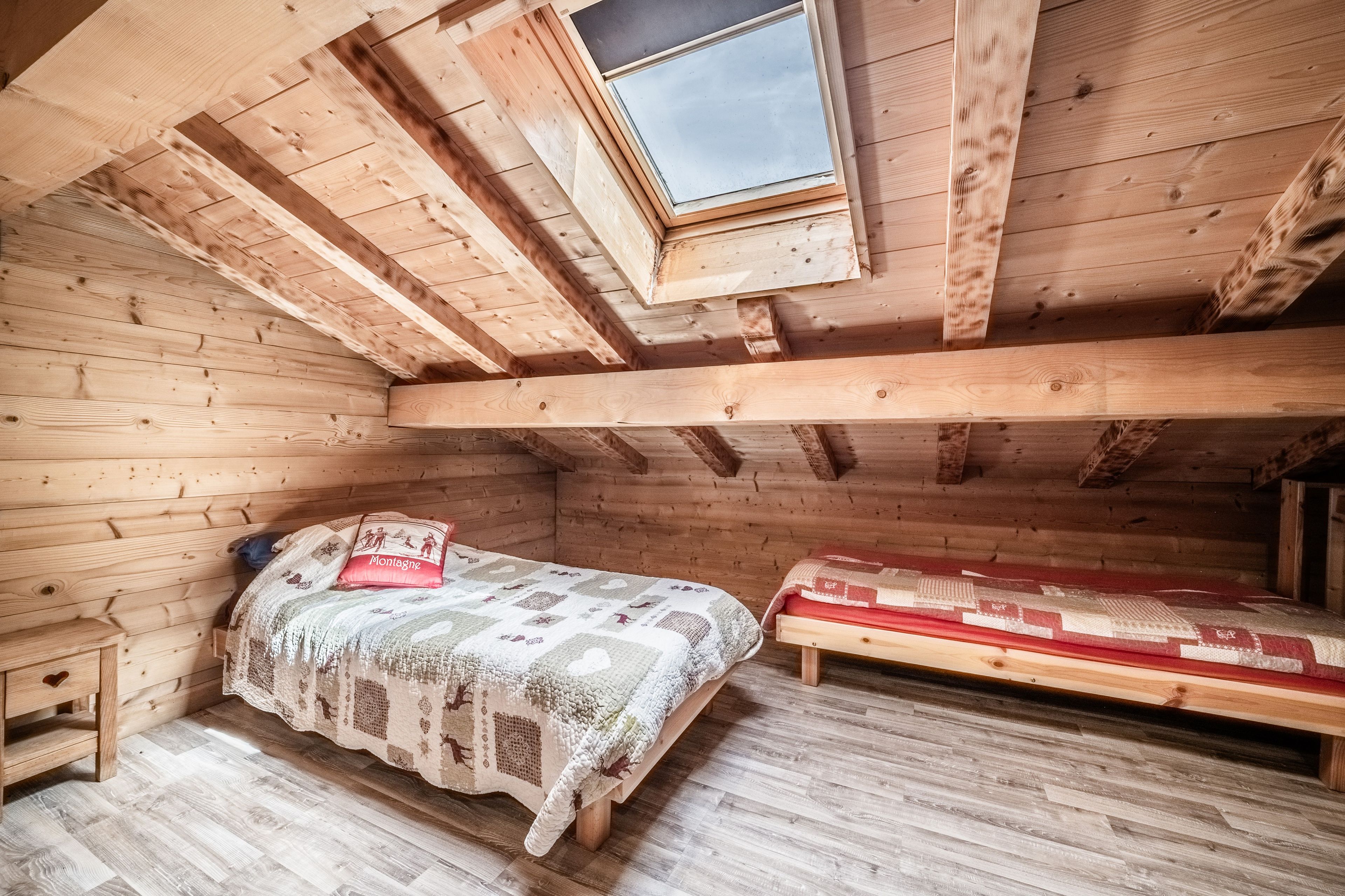 Une pièce en bois avec un plafond en pente, un lit recouvert d’une courtepointe, un banc et une petite table.