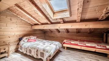Une pièce en bois avec un plafond en pente, un lit recouvert d’une courtepointe, un banc et une petite table.