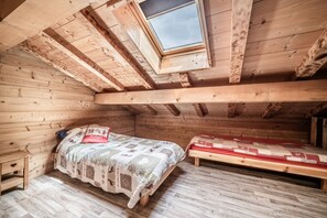 A wooden room with a sloped ceiling, a bed with a quilt, a bench, and a small table.