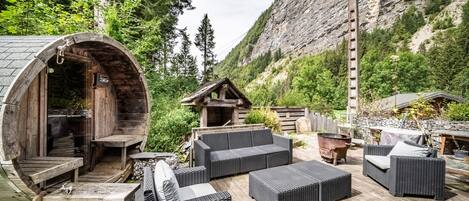 Un espacio de estar rústico al aire libre con muebles de mimbre, una pared de piedra y una estructura de madera con chimenea.