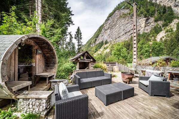 A rustic outdoor seating area with wicker furniture, a stone wall, and a wooden structure with a chimney.