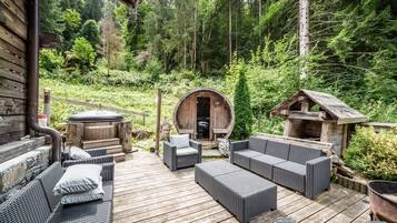 Une terrasse en bois avec des meubles en osier, un jacuzzi et une structure en forme de tonneau, le tout situé dans une zone boisée.