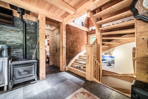 A wooden interior with a fireplace, a staircase, and a view of the outdoors.