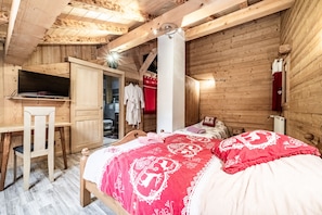 A wooden room with a bed, a desk, and a shower area.