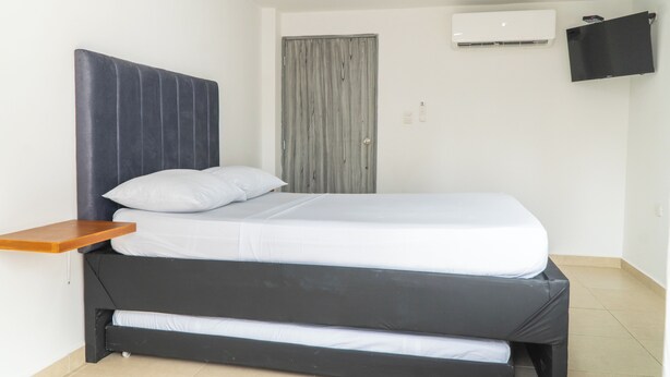 Una cama individual con cabecera, una mesita de noche, un equipo de aire acondicionado y una puerta.
