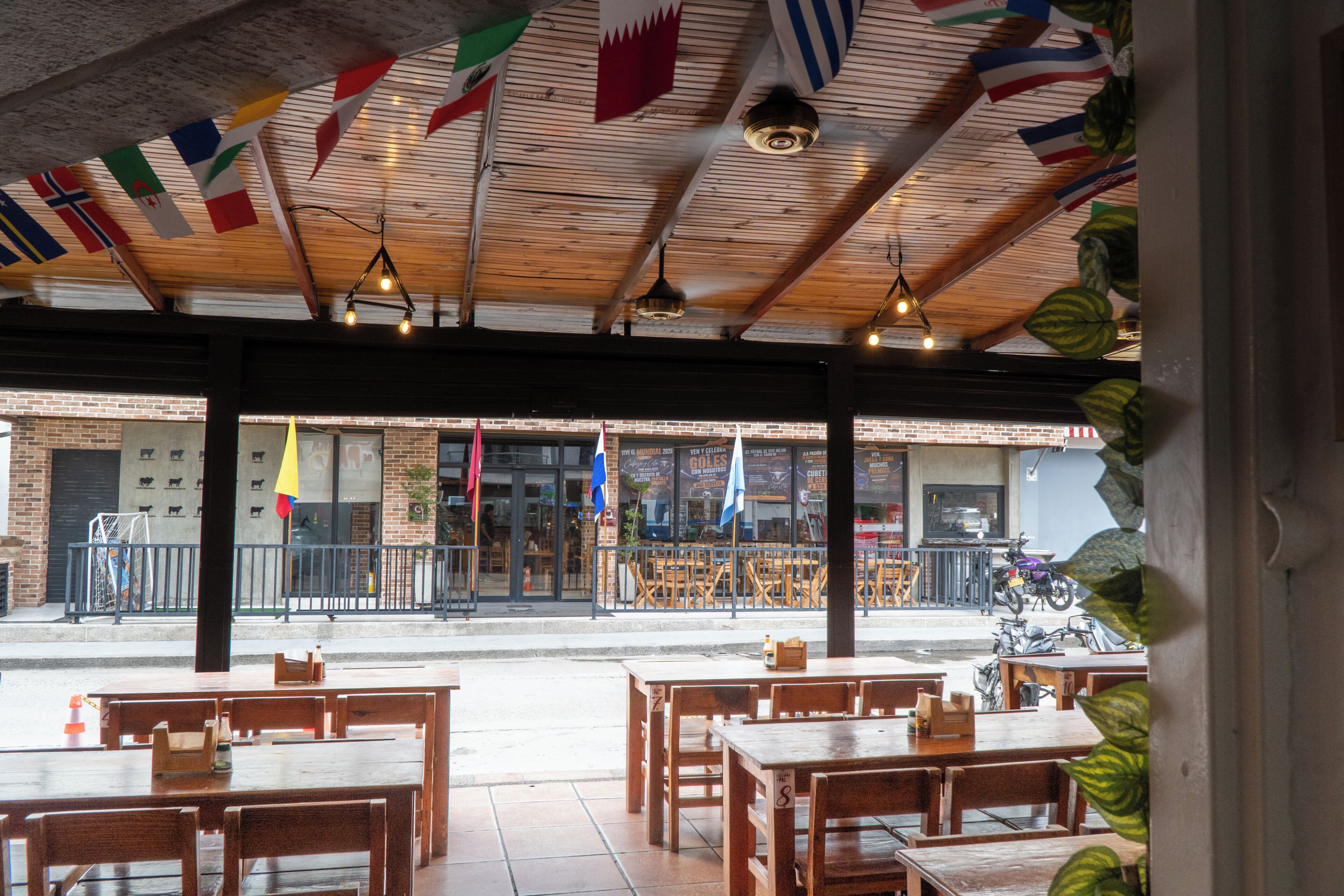 An indoor dining area with wooden tables and chairs, a brick wall, and flags hanging from the ceiling.