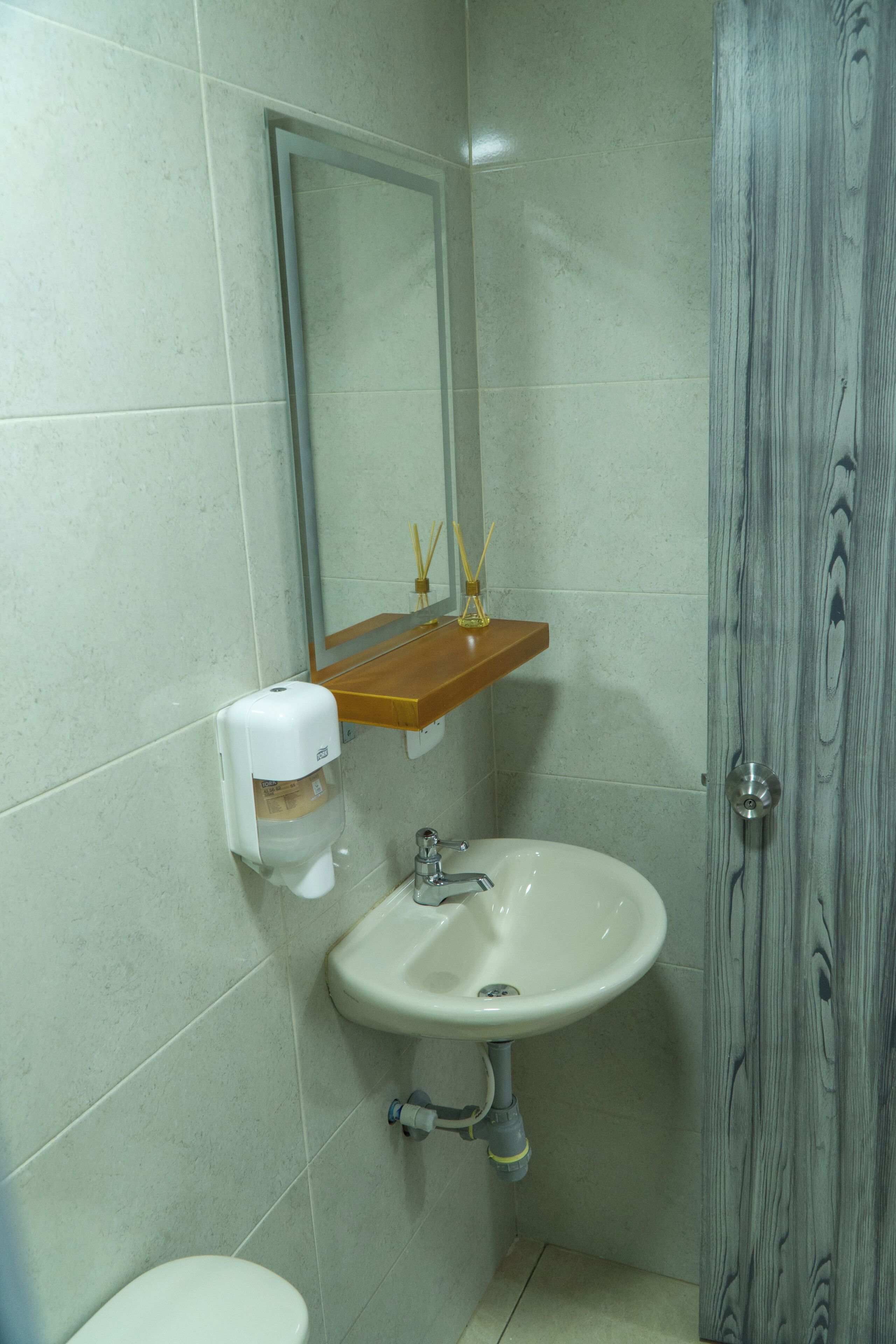 Een badkamer met een wit wastafelmeubel, een spiegel en een houten deur.