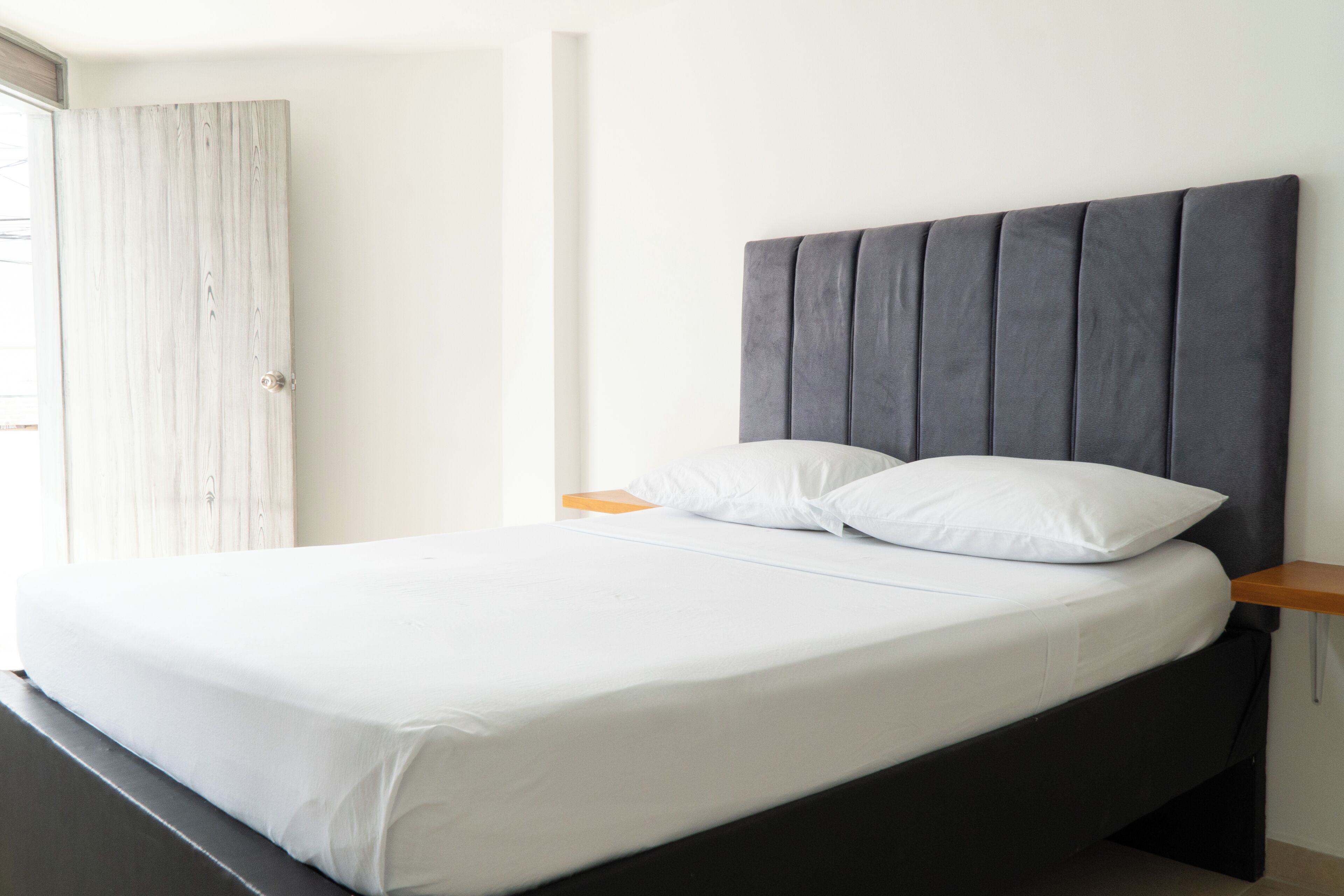 A bed with a dark headboard, white bedding, and a wooden nightstand.