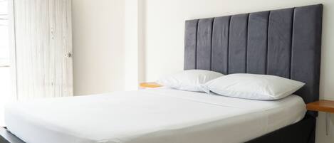A bed with a dark headboard, white bedding, and a wooden nightstand.