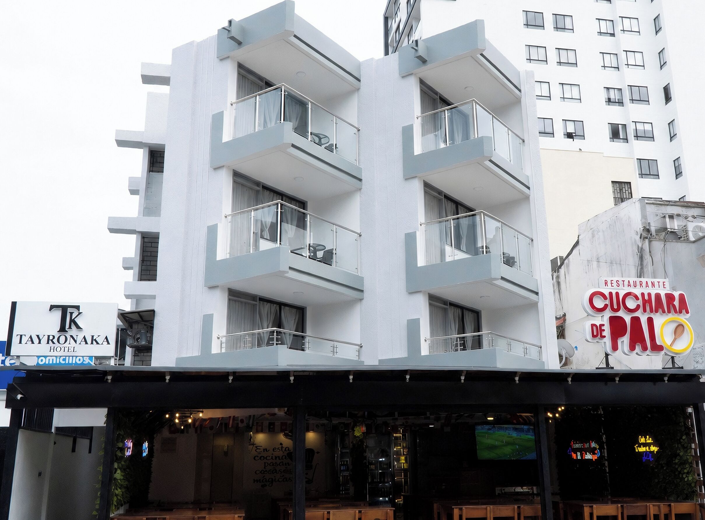 Um hotel com vários andares, varandas, um letreiro de restaurante e o interior do restaurante visível.