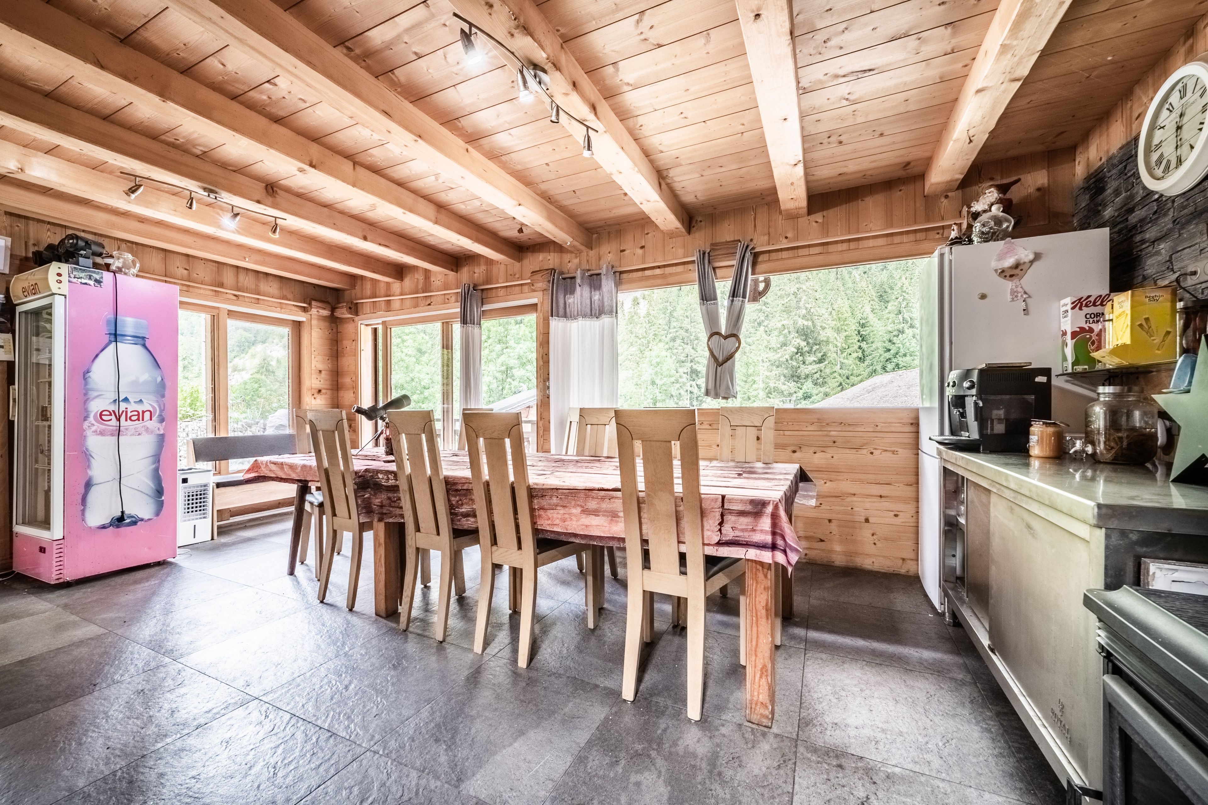 Un intérieur en bois comprenant une table à manger, des chaises, un réfrigérateur et un distributeur d’eau.