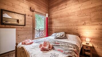 Une chambre dans un chalet en bois, avec un lit, une table de chevet, une fenêtre donnant sur la verdure et un radiateur.