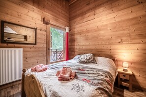 A wooden cabin room with a bed, a nightstand, a window with a view of greenery, and a radiator. - Bed and Breakfast 'Chambre Edelweiss' with Mountain View, Wi-Fi and Air Conditioning (Morzine)