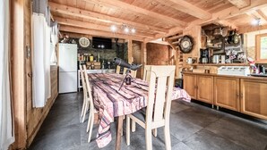 A wooden interior with a dining table, chairs, a kitchen area with cabinets and appliances, and a clock on the wall.
