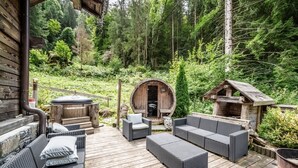 A wooden deck with wicker furniture, a hot tub, and a barrel-shaped structure in a forested area.