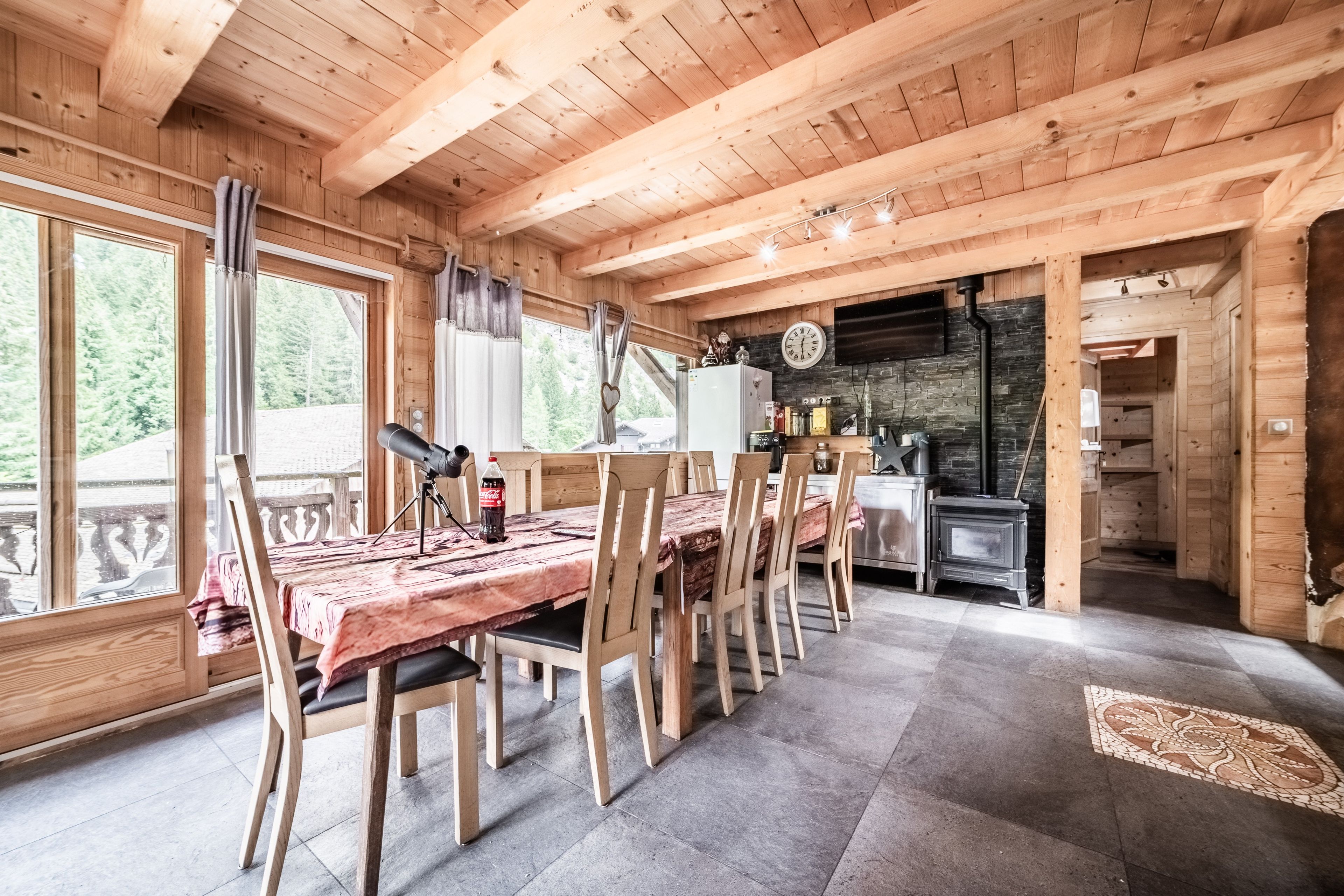 L’intérieur d’un chalet en bois comprend un coin repas, une cuisine et une grande fenêtre donnant sur une forêt.