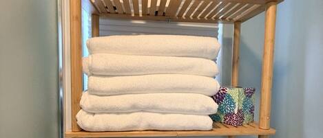 A wooden shelf with stacked white towels and a basket of toiletries.