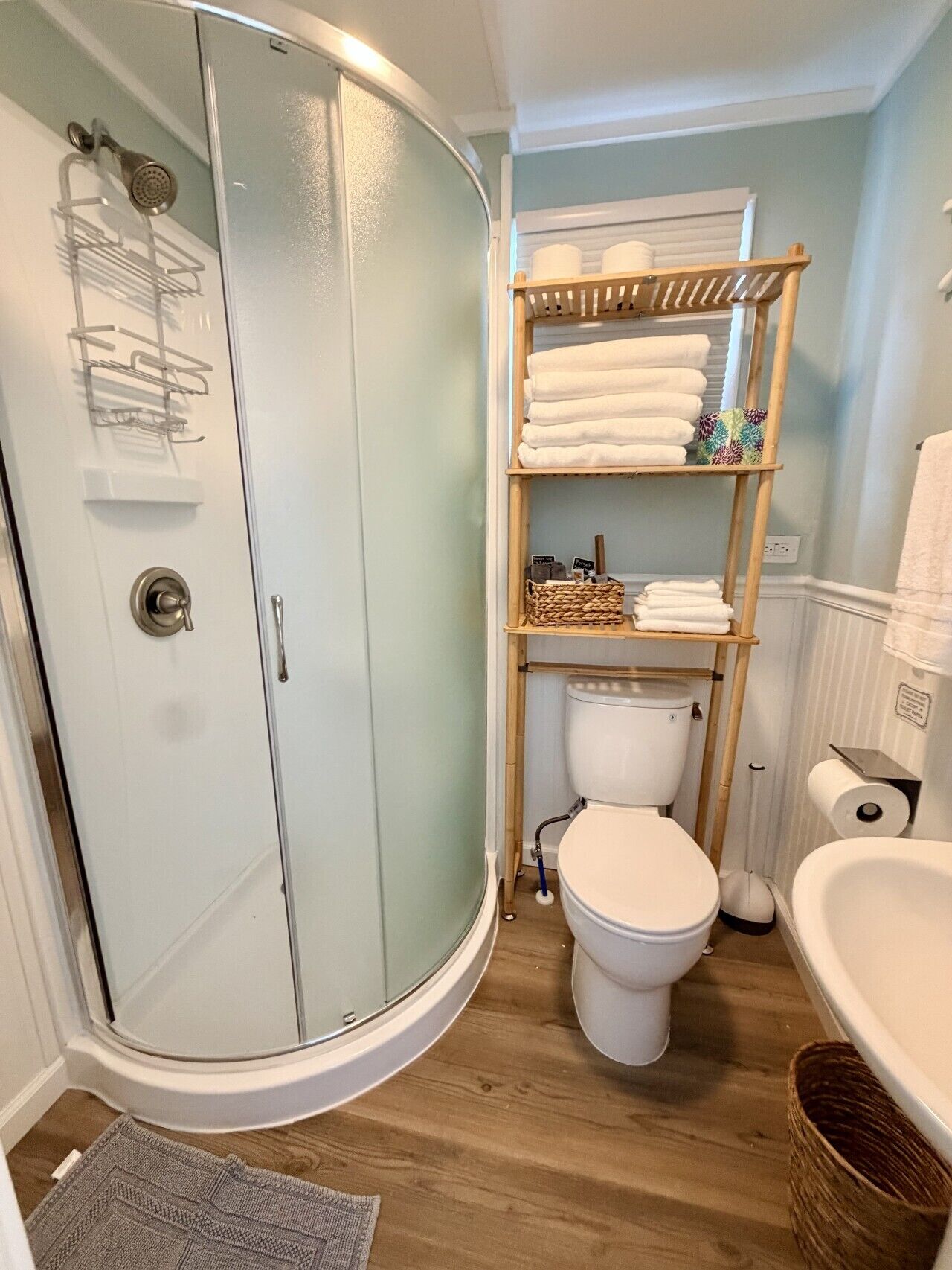 Een badkamer met een douche in een glazen cabine, een toilet, een wastafel en een plank met handdoeken en toiletartikelen.