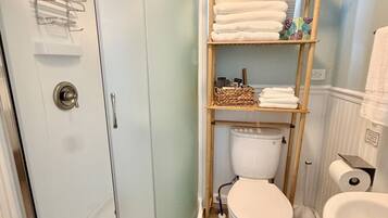 Een badkamer met een douche in een glazen cabine, een toilet, een wastafel en een plank met handdoeken en toiletartikelen.