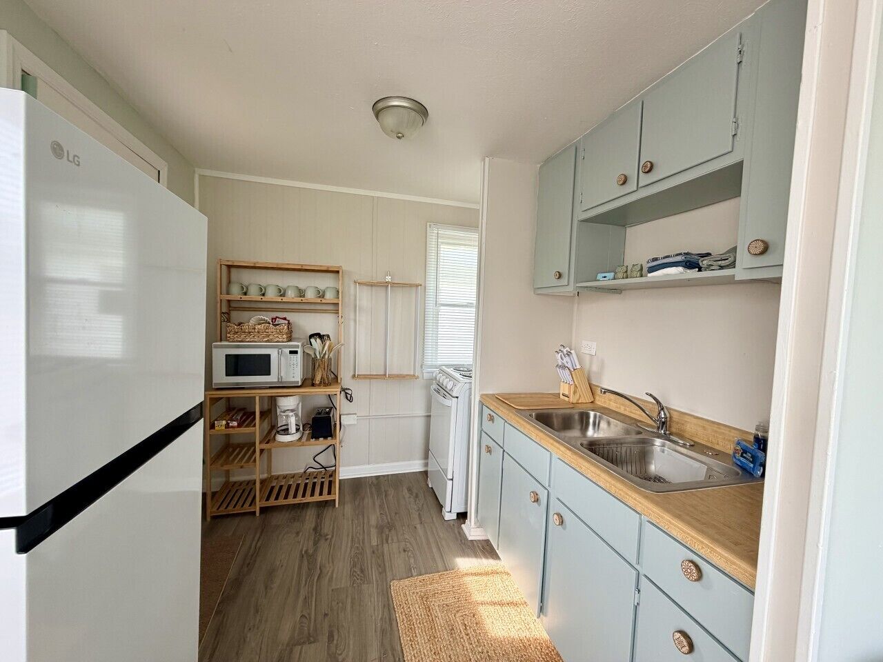 A compact kitchen with a white refrigerator, microwave, and stove, wooden shelves, and light blue cabinets.