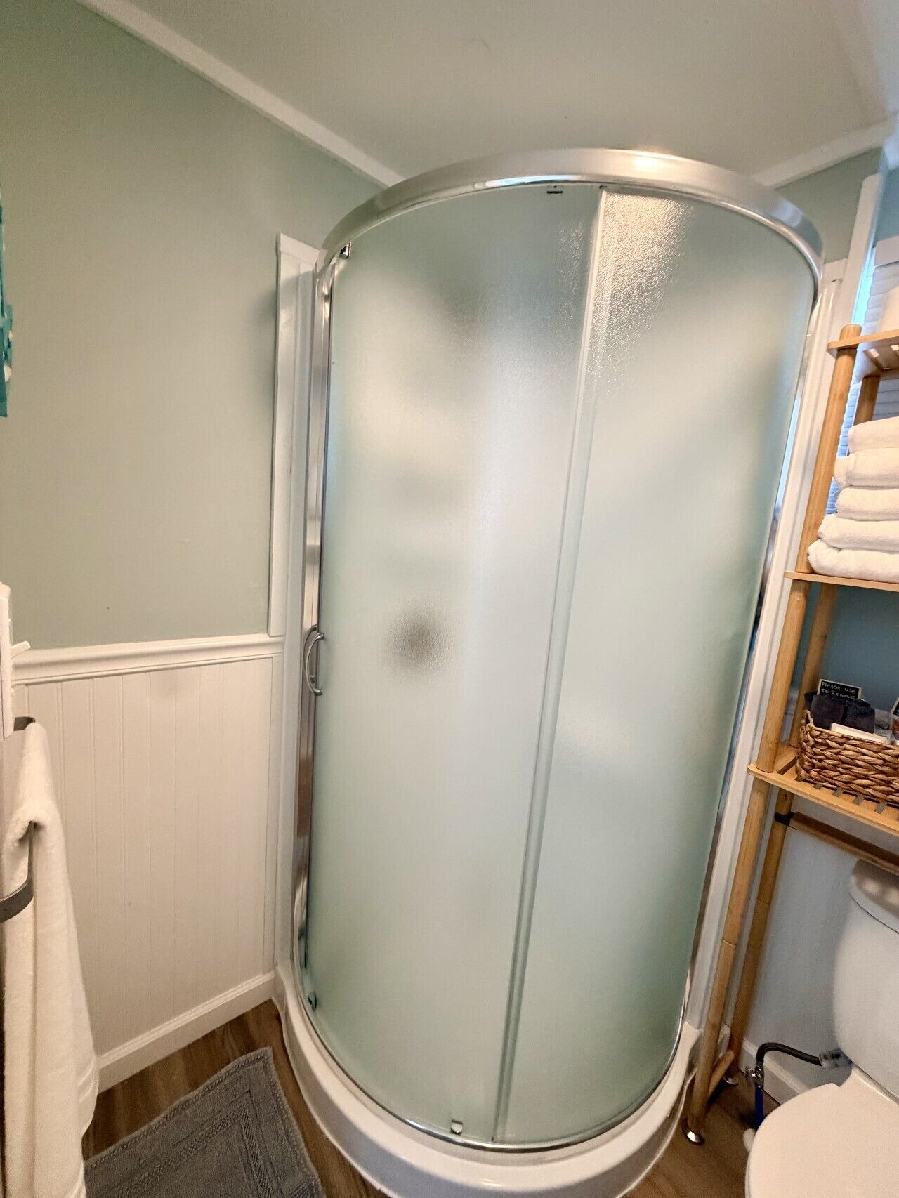 A bathroom with a glass-enclosed shower, a white toilet, and a wooden shelf with towels.