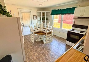 Cocina compacta con mesa, sillas, refrigerador, estufa y ventana con vista a un jardín.