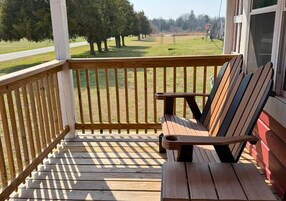 Una terraza de madera con un banco y vistas a un campo cubierto de césped y árboles.