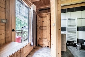 A wooden cabin interior with a wooden door, a bench, and a view of a mountain landscape.