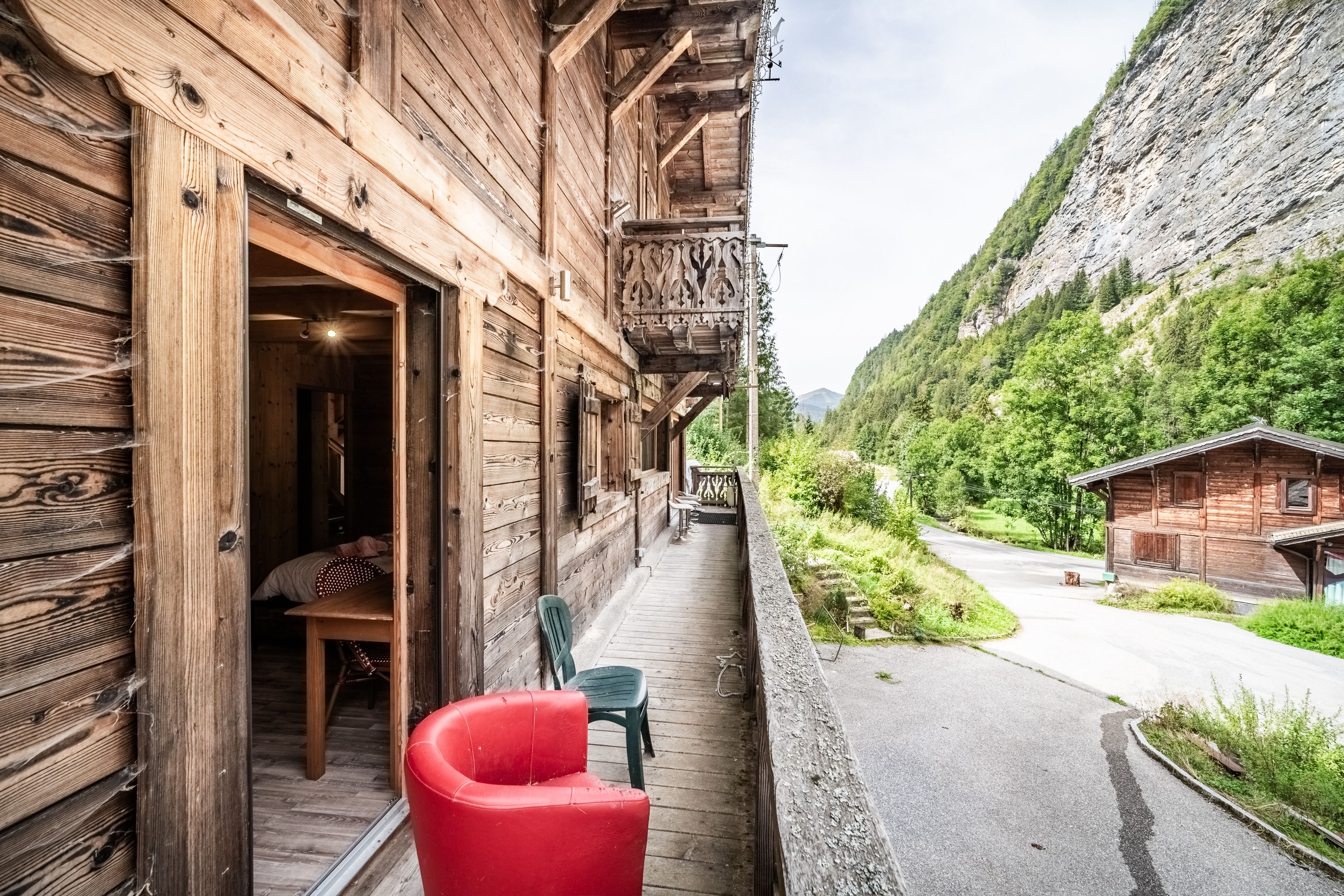 Un bâtiment en bois doté d’un balcon, d’une chaise rouge et offrant une vue sur une montagne.
