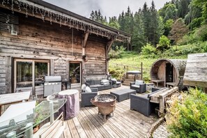 A wooden cabin with a deck, outdoor seating, a barbecue grill, and a wood stove.