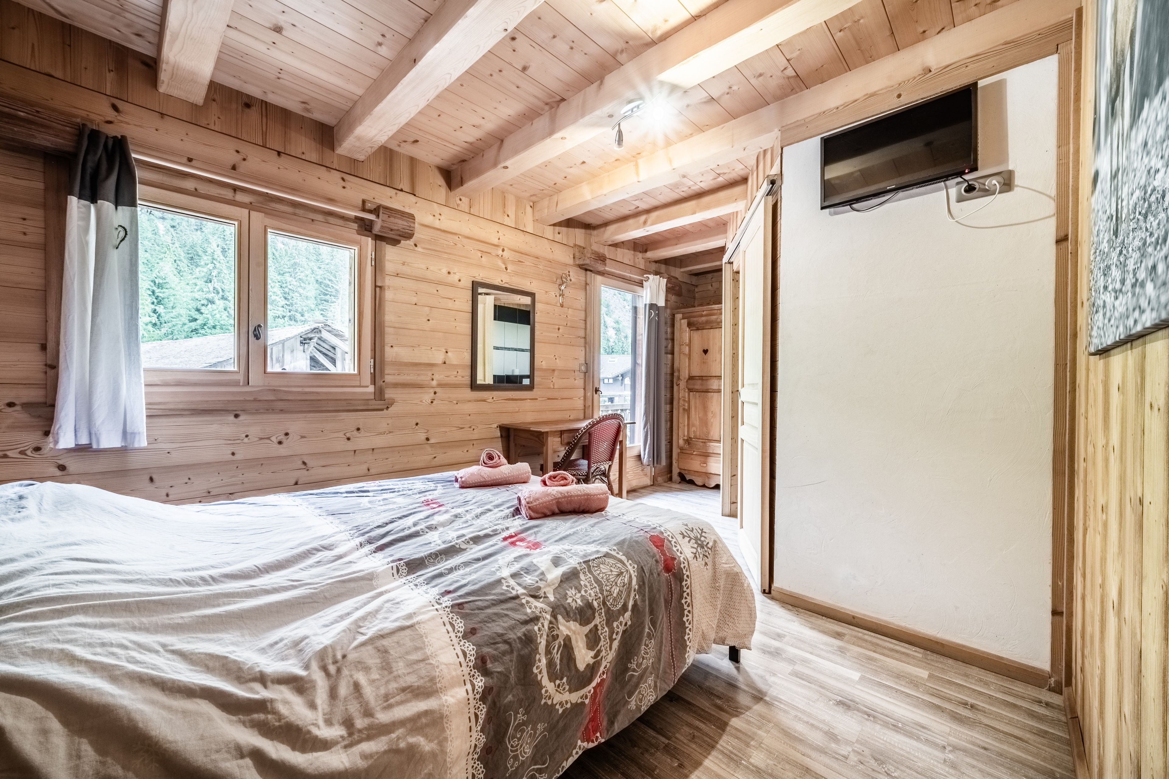 Ein Zimmer in einer Holzhütte mit einem Bett, einem Stuhl, einem Fenster und einer Tür.