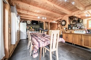 A wooden interior with a dining table, chairs, a kitchen area with cabinets and appliances, and a clock on the wall.