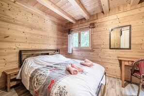 A wooden cabin room with a bed, a chair, and a window.
