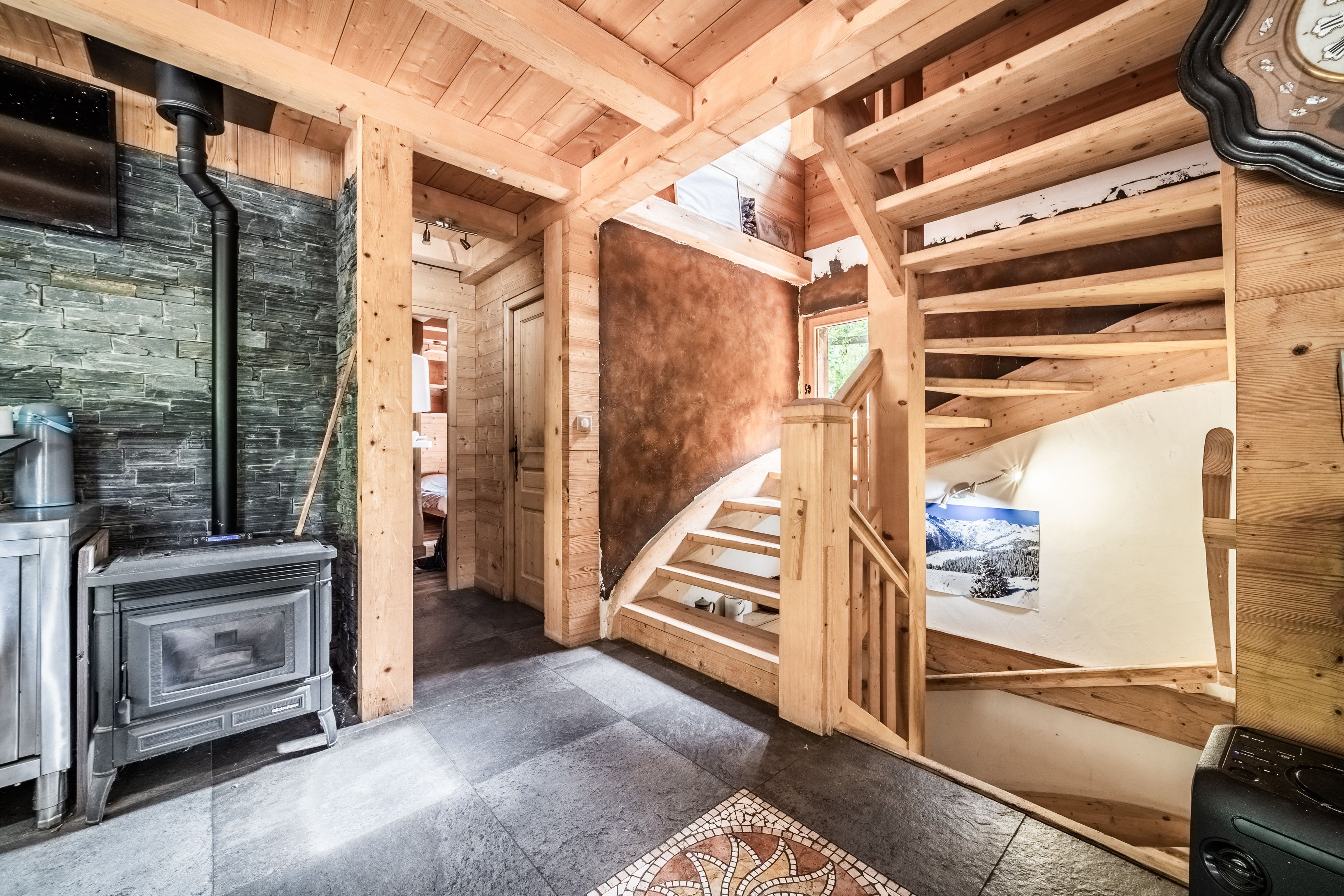 Un intérieur en bois avec une cheminée, un escalier et une vue sur l’extérieur.