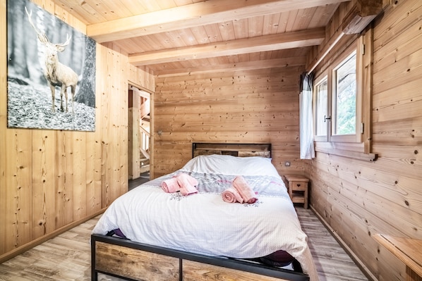 A wooden cabin bedroom with a bed, a nightstand, and a window.