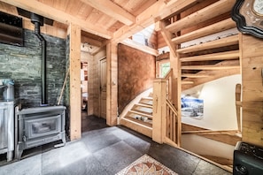 A wooden interior with a fireplace, a staircase, and a view of the outdoors.