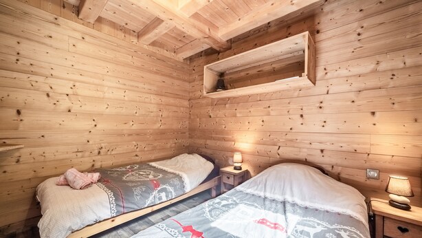 Een houten kamer met twee bedden, een plank en een nachtkastje met een lamp.