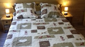 Una cama con colcha de motivos de animales y corazones, flanqueada por dos lámparas de noche en mesitas de madera.