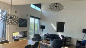 Een moderne woonkamer met een houten eettafel, grijze banken en een aan de muur bevestigde televisie.