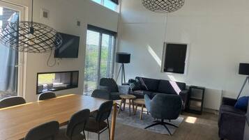 Ein modernes Wohnzimmer mit einem Holzespeisetisch, grauen Sofas und einem an der Wand befestigten Fernseher.