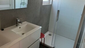 Een badkamer met een wit wastafel, een spiegel, een douche en een rode kruk.