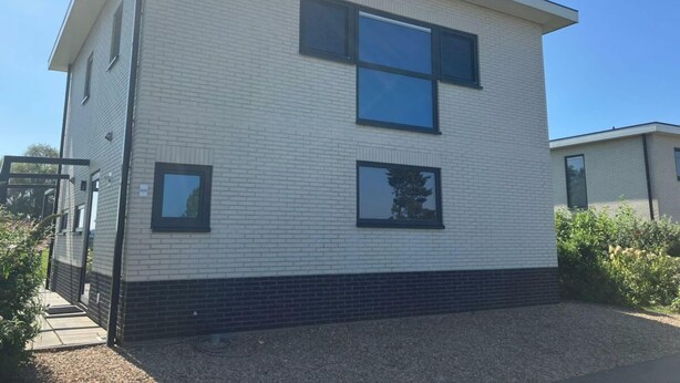 Een modern gebouw met twee verdiepingen, een plat dak, grote ramen en een gevel van baksteen.