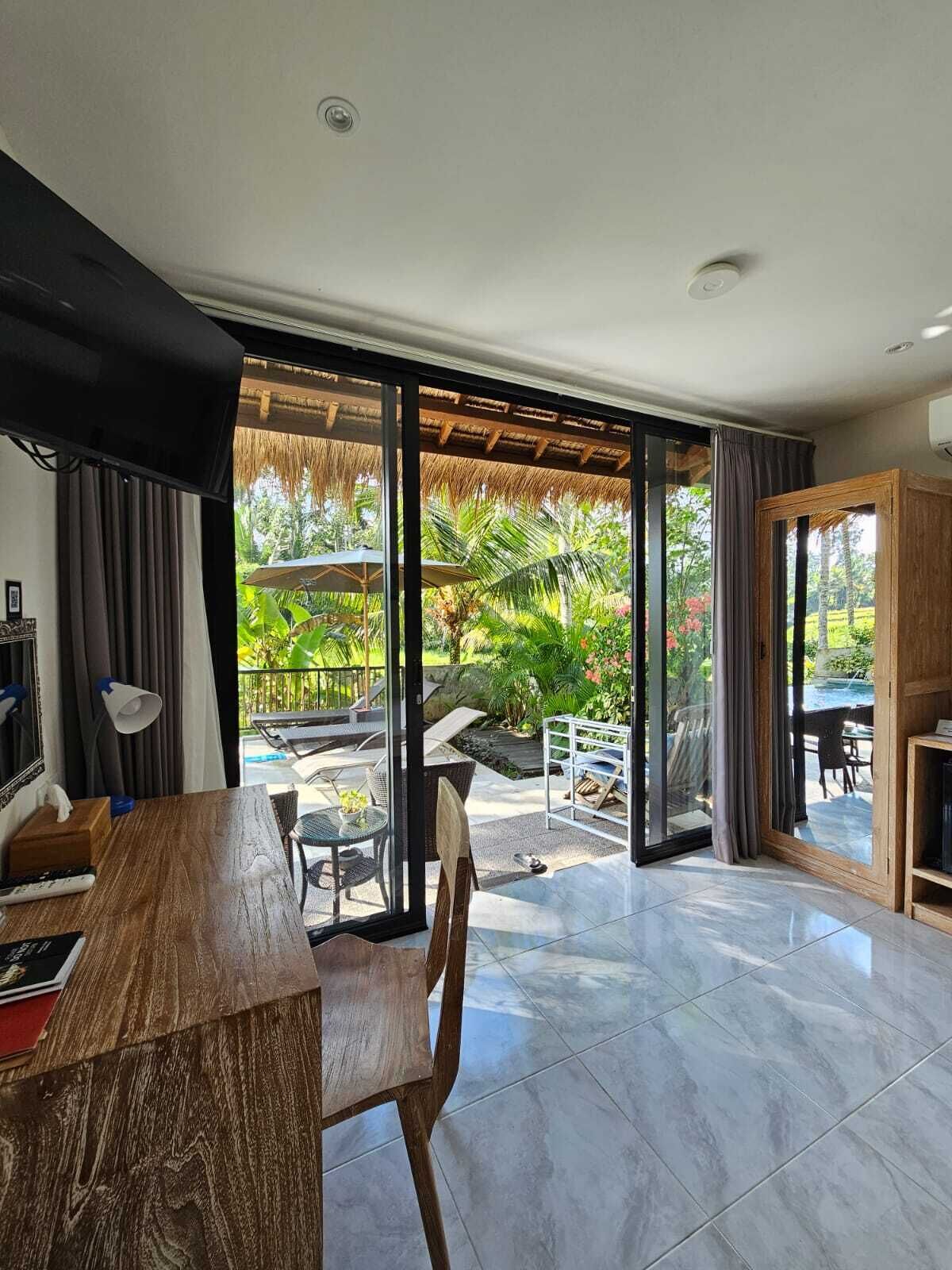 Une chambre moderne dotée d’un coin repas et d’une grande porte-fenêtre coulissante donnant sur un espace extérieur avec une piscine et des plantes tropicales.