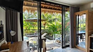 Une chambre moderne dotée d’un coin repas et d’une grande porte-fenêtre coulissante donnant sur un espace extérieur avec une piscine et des plantes tropicales.