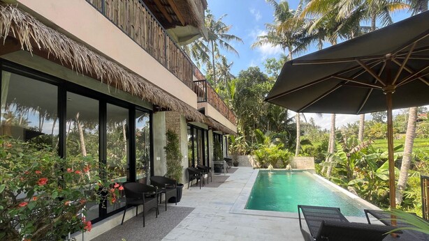 A poolside area with a pool, lounge chairs, and a thatched roof structure.