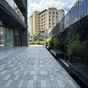 Un passeig urbà modern amb sòl de rajola, tanca metàl·lica i un edifici al fons amb el rètol de Mayfair Insurance.