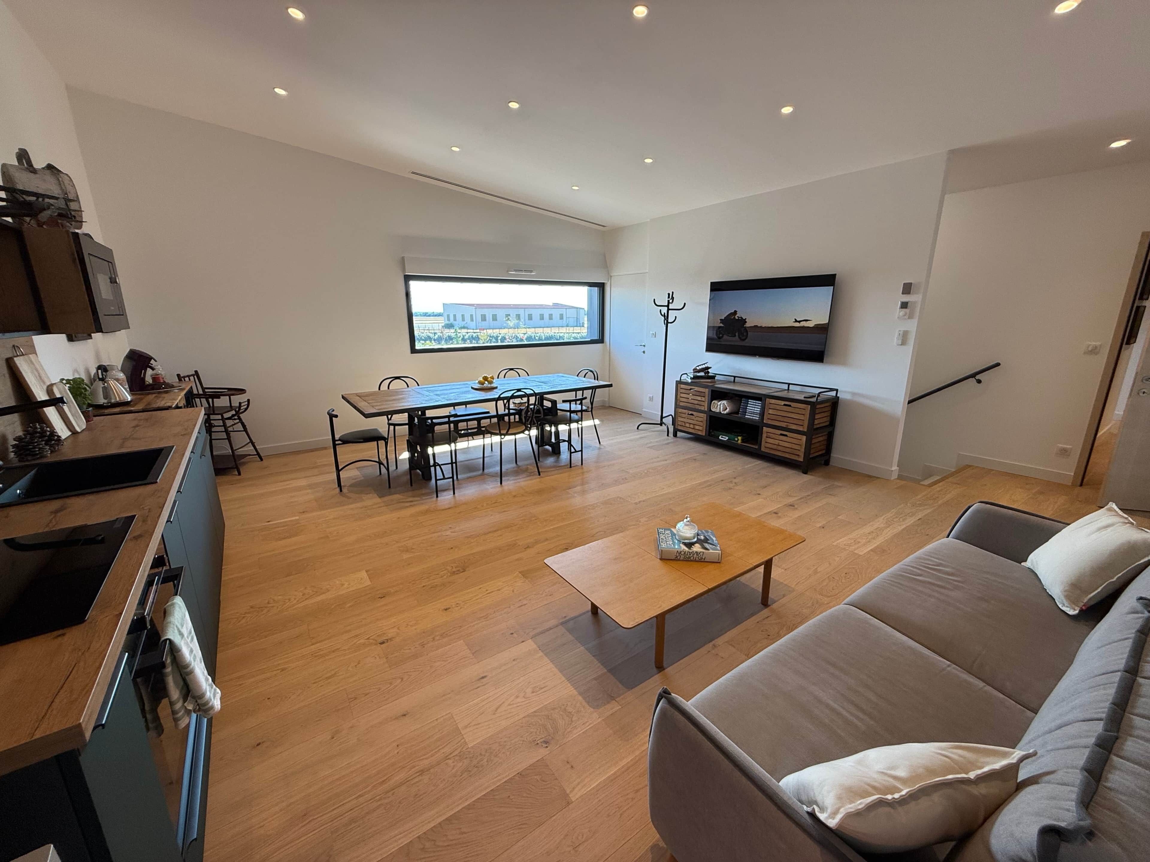 Una sala de estar moderna con comedor, un sofá, una mesa de centro y un televisor montado en la pared.